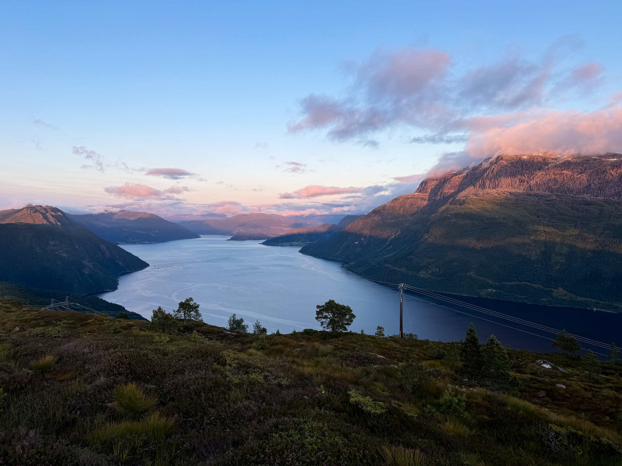 Fjord at dusk seen from the mountainside, with pink evening clouds.