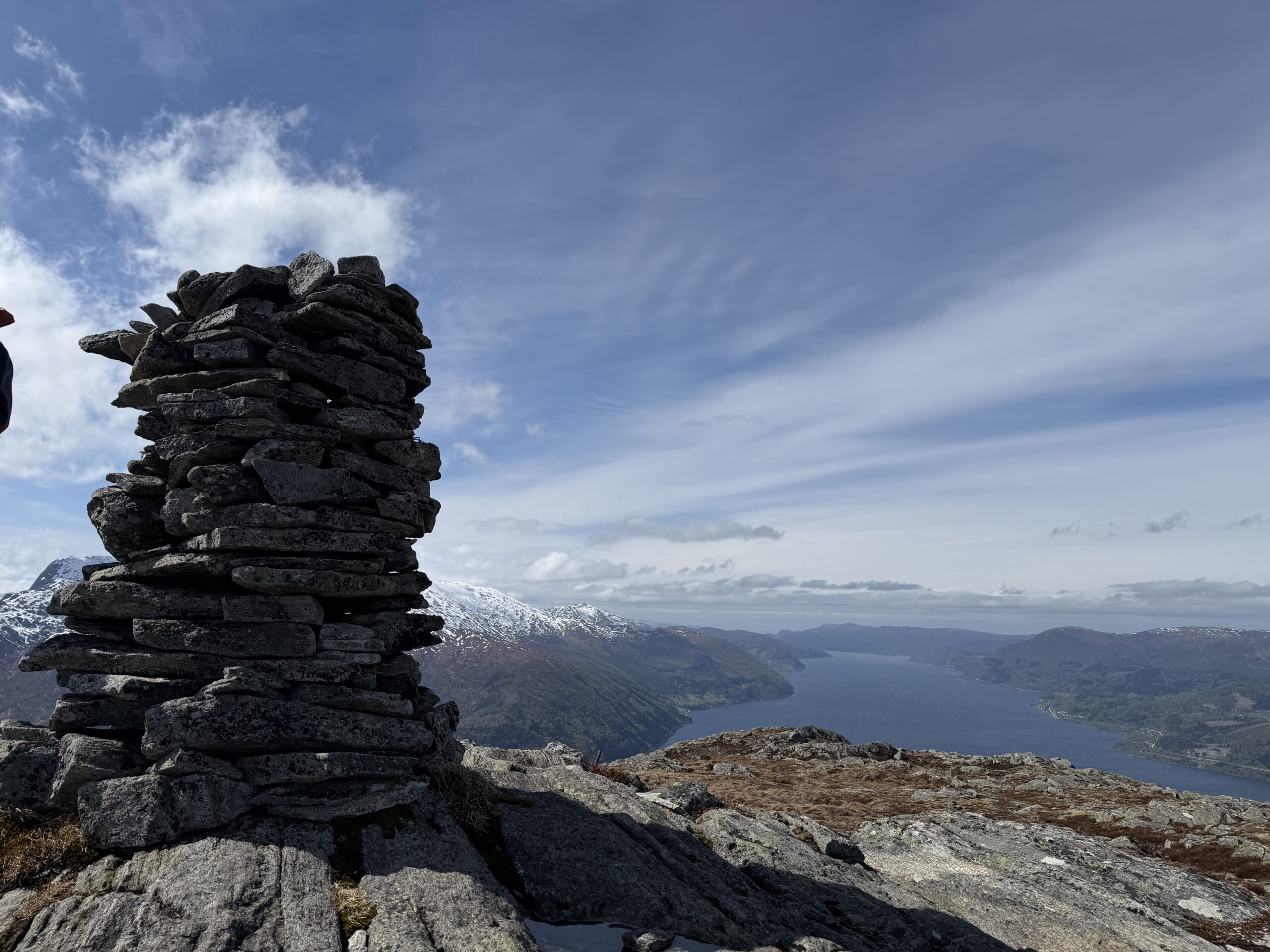 Stone cairn on a mountain summit overlooking a fjord.