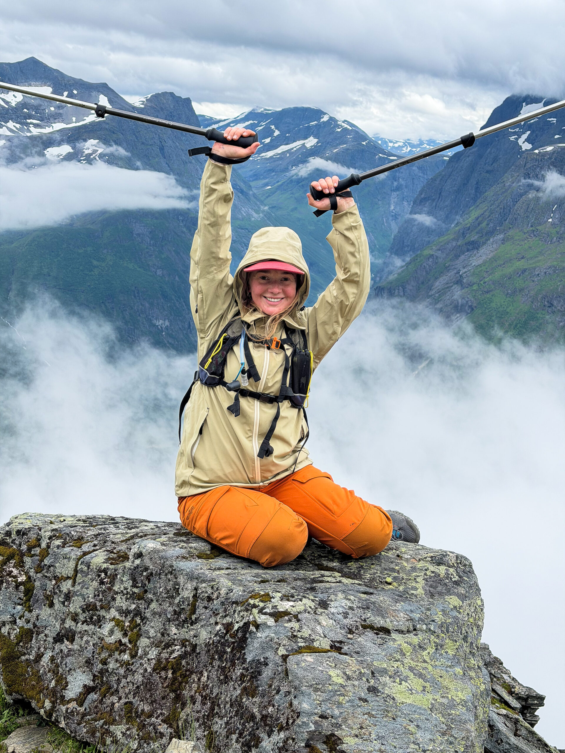 Hiker cheering with trekking poles raised on a rocky summit above the clouds.