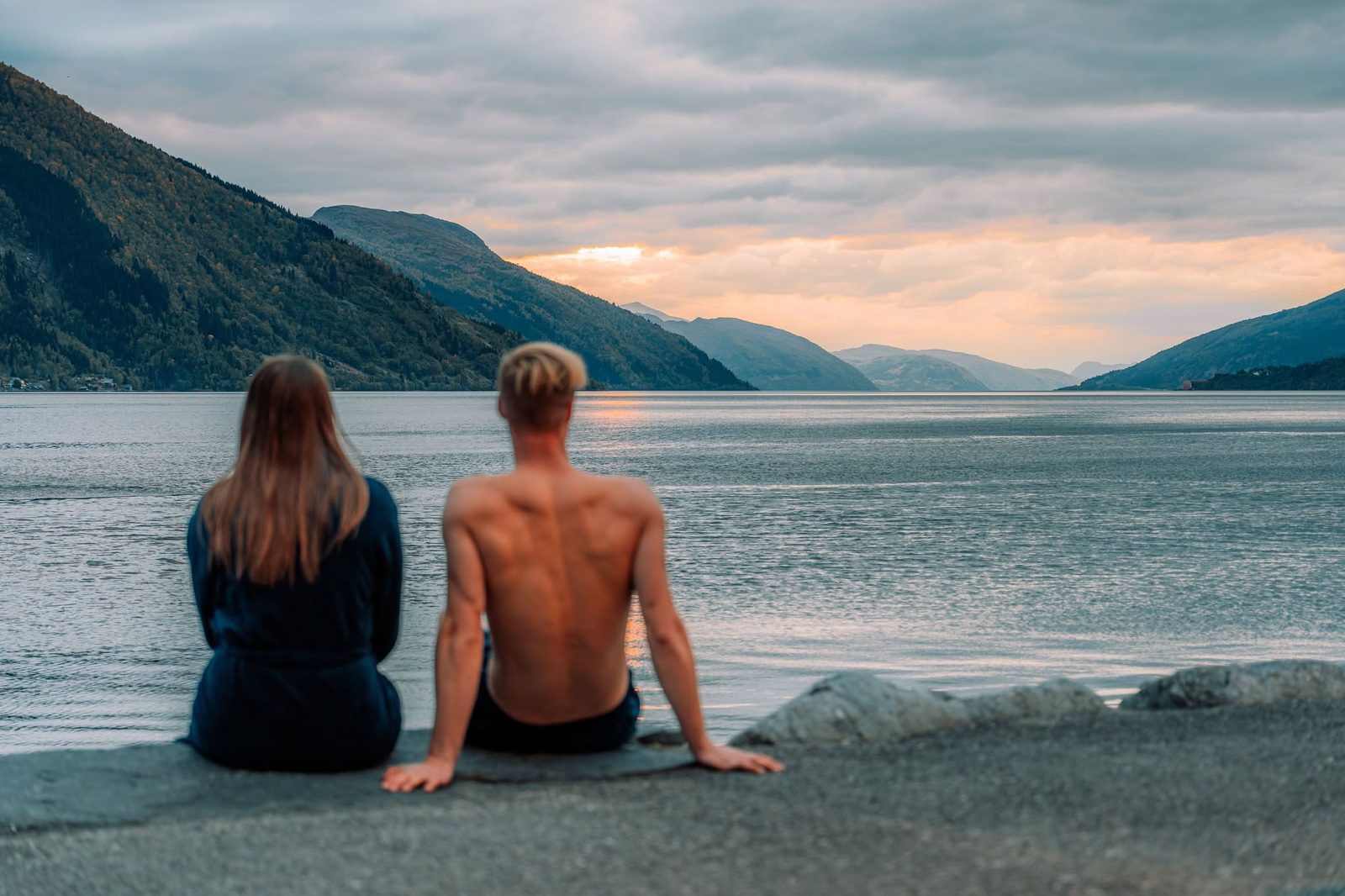 Two guests sitting by the fjord outside Badestova after the sauna, in the evening light