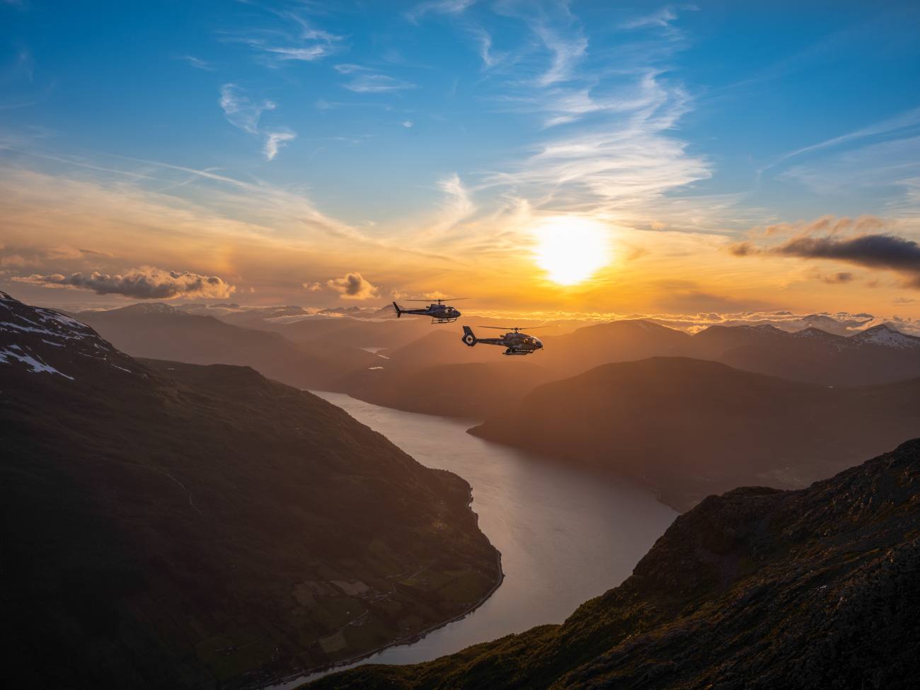 Two helicopters flying over Nordfjord at sunset.