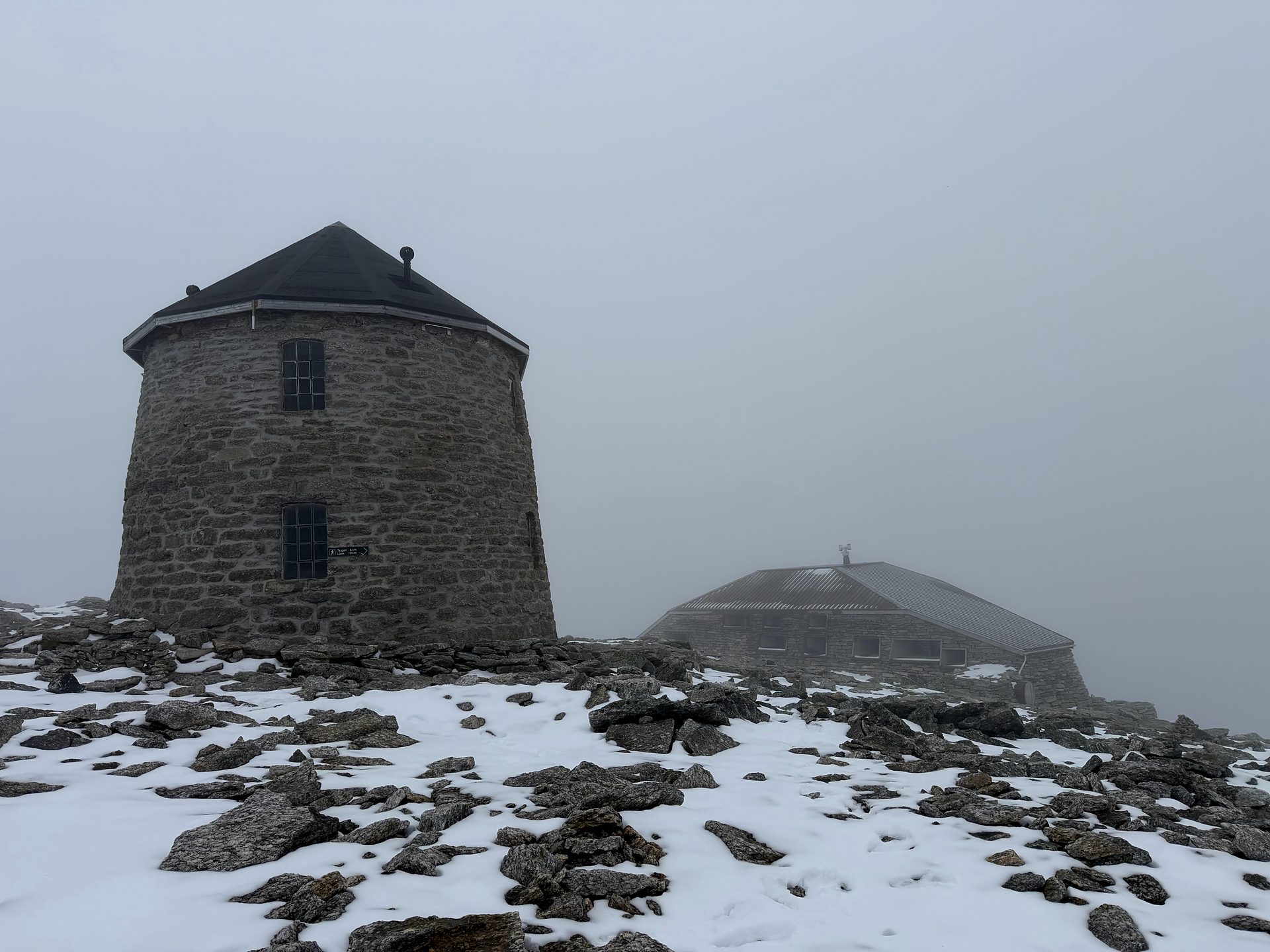 The stone tower Skålatårnet and the Skålabu cabin at the top of Skåla, in fog with fresh snow.