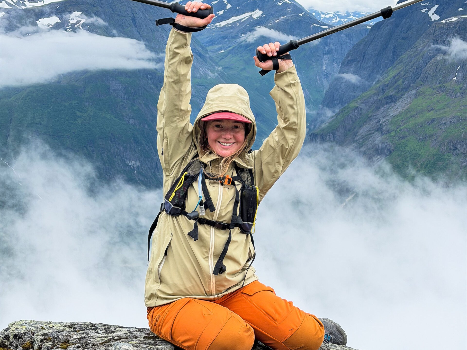 Hiker celebrating on Slogen, with clouds and the Sunnmøre Alps behind.