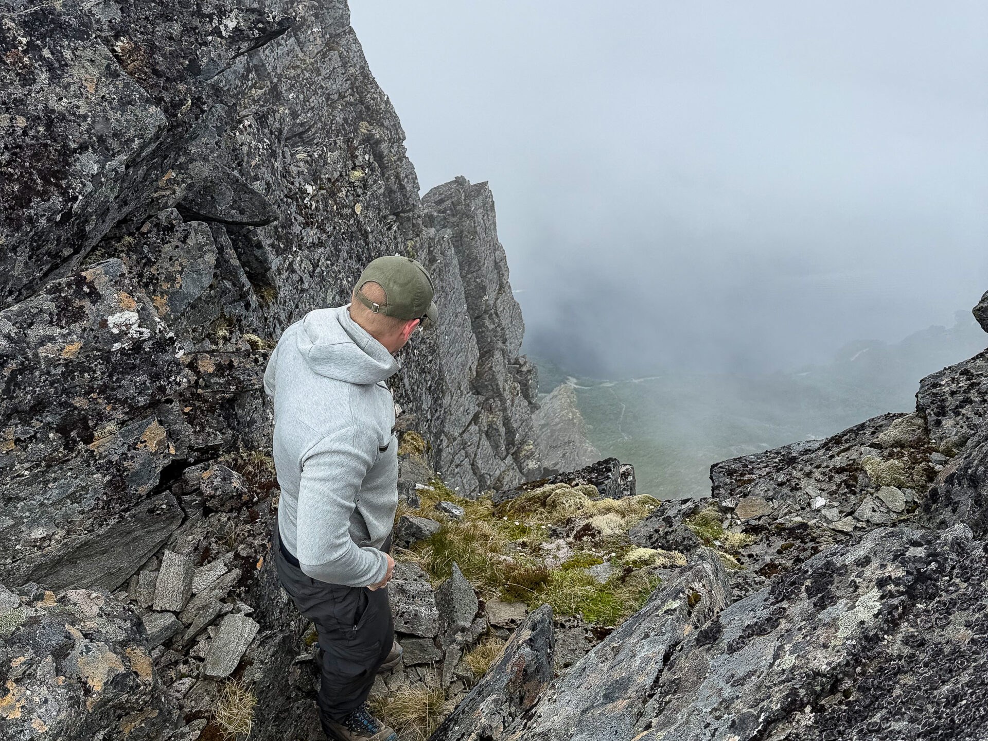 Hiker looking down a steep, rocky passage on Slogen, with low cloud covering the valley below.